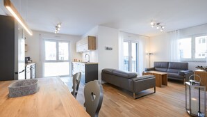A modern living room with a wooden dining table, grey sofa, and a small kitchen area with white cabinets. - Newly built holiday apartment in a top location in Garmisch-Partenkirchen (Garmisch-Partenkirchen)