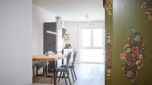 A modern kitchen with a wooden dining table, chairs, and a bench. There is a refrigerator, a coffee maker, and a window providing natural light. - Newly built holiday apartment in a top location in Garmisch-Partenkirchen (Garmisch-Partenkirchen)