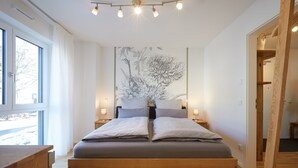 A modern bedroom with a large bed, bedside tables, a wall-mounted artwork, and a wooden floor. - Newly built holiday apartment in a top location in Garmisch-Partenkirchen (Garmisch-Partenkirchen)