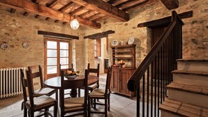 A rustic dining area with a wooden table and chairs, a staircase with a wooden railing, and a stone wall with a window. - HAMLET THE POET - LODGE HOUSE (Umbria)