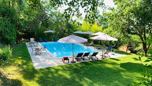A swimming pool with lounge chairs and umbrellas, surrounded by lush greenery. - HAMLET THE POET - LODGE HOUSE (Umbria)