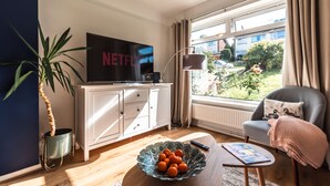 Ein Wohnzimmer mit Fernseher, einer Orangenschale, einer Pflanze und Blick ins Freie.