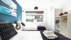 Ein modernes Hotelzimmer mit einem großen Bett, einem Kleiderschrank, einem Fenster mit Blick auf Gebäude und einem Bild an der Wand.