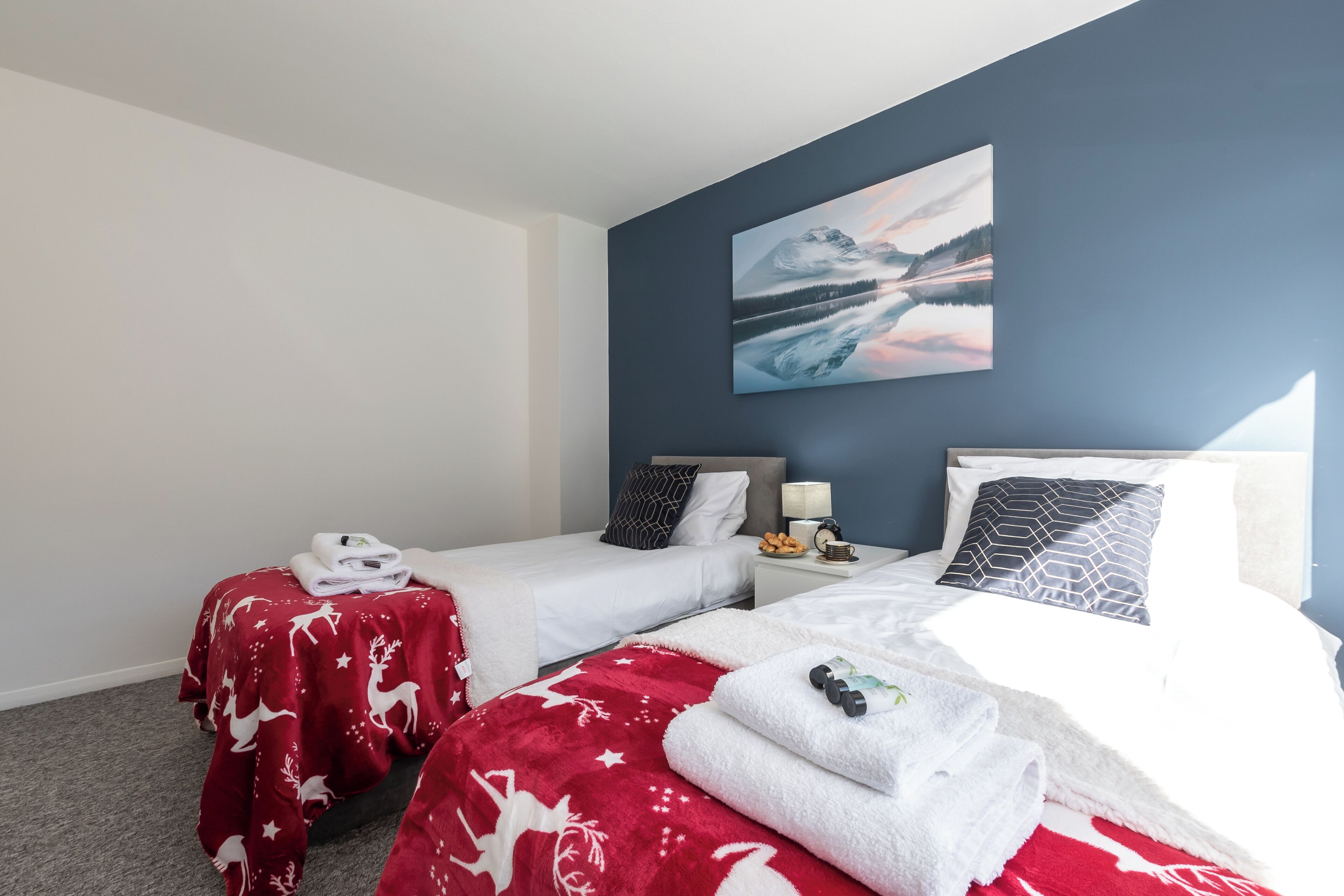 Ein Hotelzimmer mit zwei Betten, jedes mit einer roten und weißen Decke, einem Nachttisch mit einer Lampe und einem Bild an der Wand.