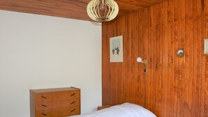 Une chambre avec des murs lambrés en bois, une commode en bois, un lit avec une literie blanche et un luminaire fixé au mur.