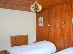 Un dormitorio con paredes de madera panelada, un aparador de madera, una cama con ropa de cama blanca y un aplique de pared.