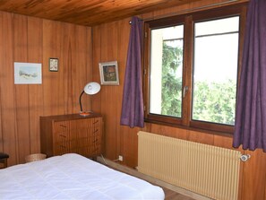 Una stanza con pannelli in legno, un letto, una scrivania con una lampada e una finestra con tende.