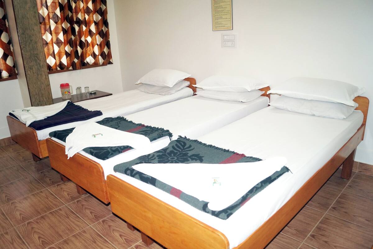 A room with three wooden beds, each with white bedding and decorative throw pillows.