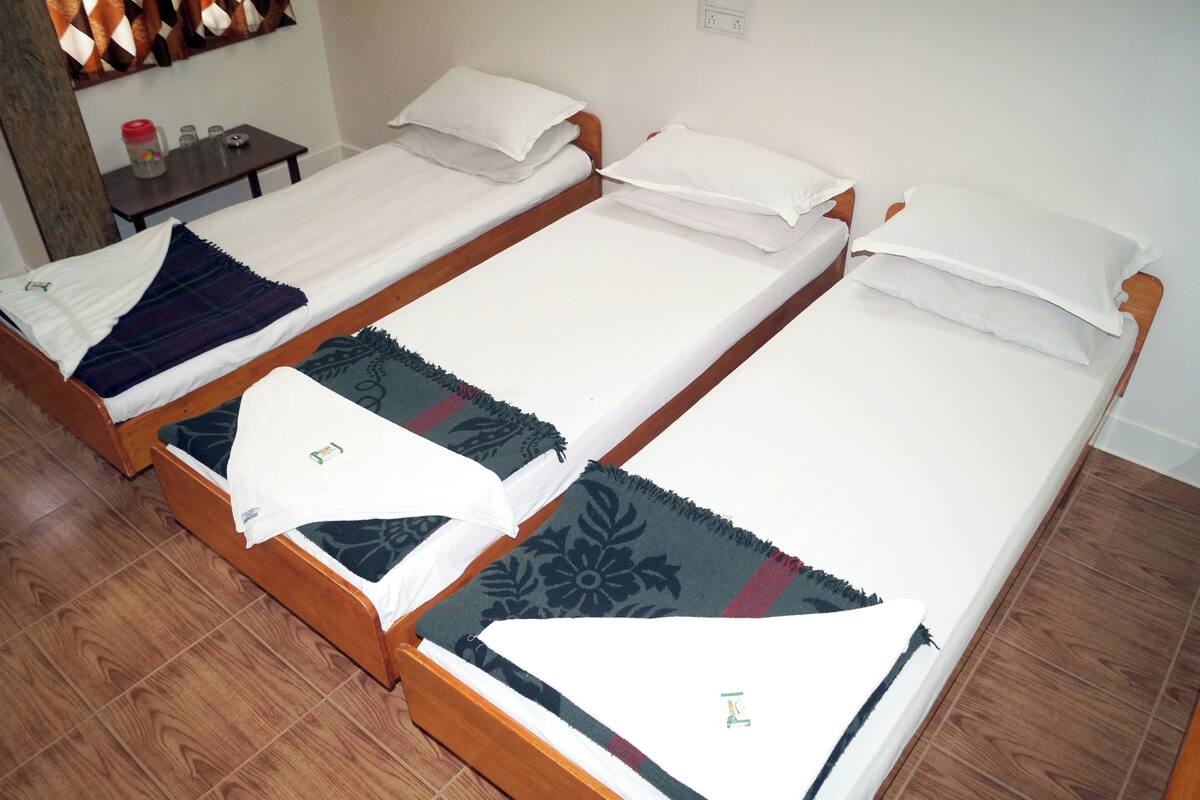 A room with three wooden beds, each with white bedding and decorative pillows. There is a small table with a red container and a few items on it.