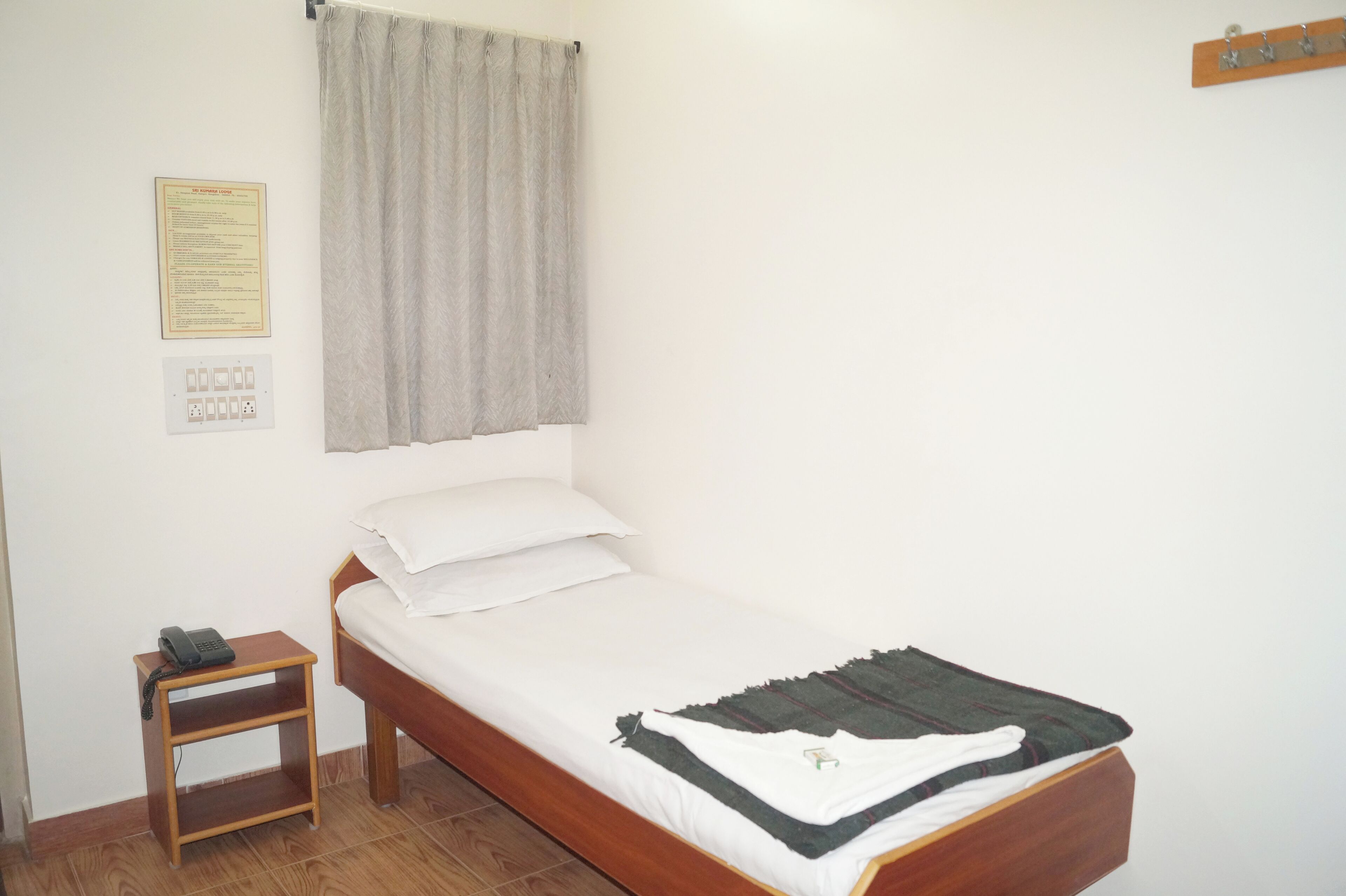 Una cama individual con estructura de madera, colchón blanco y cortina gris.