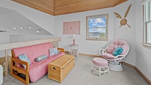 Une pièce chaleureuse avec un plafond en bois, un canapé rose, une commode en osier, une chaise blanche et une petite table.