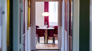A hallway leading to a dining area with a table and chairs, a pendant light, and a window with curtains. - Gem Suites Holiday Apartments (Augustenborg)