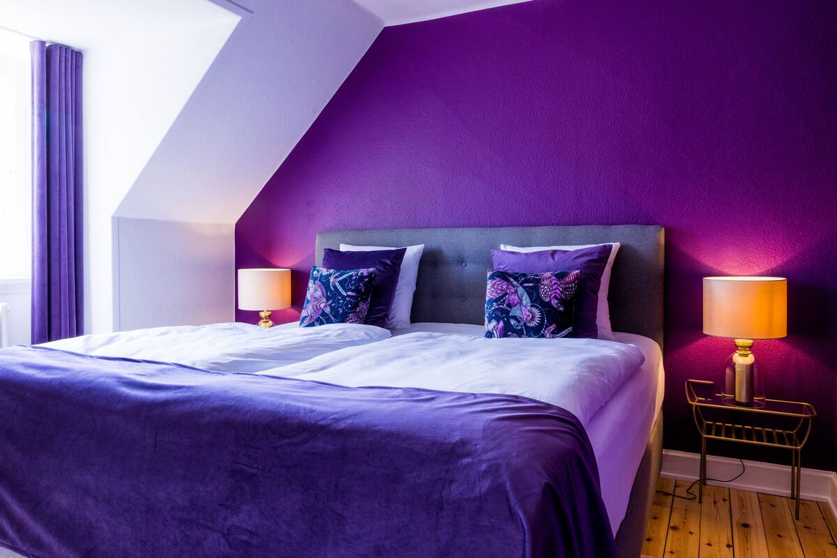 A bedroom with a large bed, purple walls, and two bedside lamps.