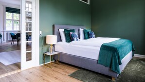 A bedroom with a bed, bedside table, and a view of a dining area. - Gem Suites Holiday Apartments (Augustenborg)