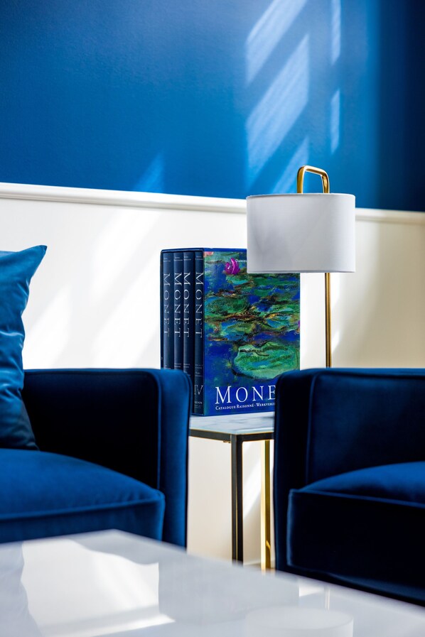 Ein Zimmer mit einem blauen Sofa, einem kleinen Tisch, einer Lampe und einem Buch von Monet an der Wand.