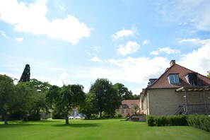 A building with a red-tiled roof, a stone facade, and a grassy courtyard.