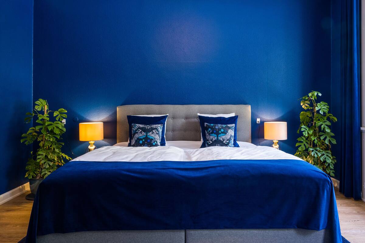 A bed with a grey headboard, blue bedding, and two matching lamps on either side.