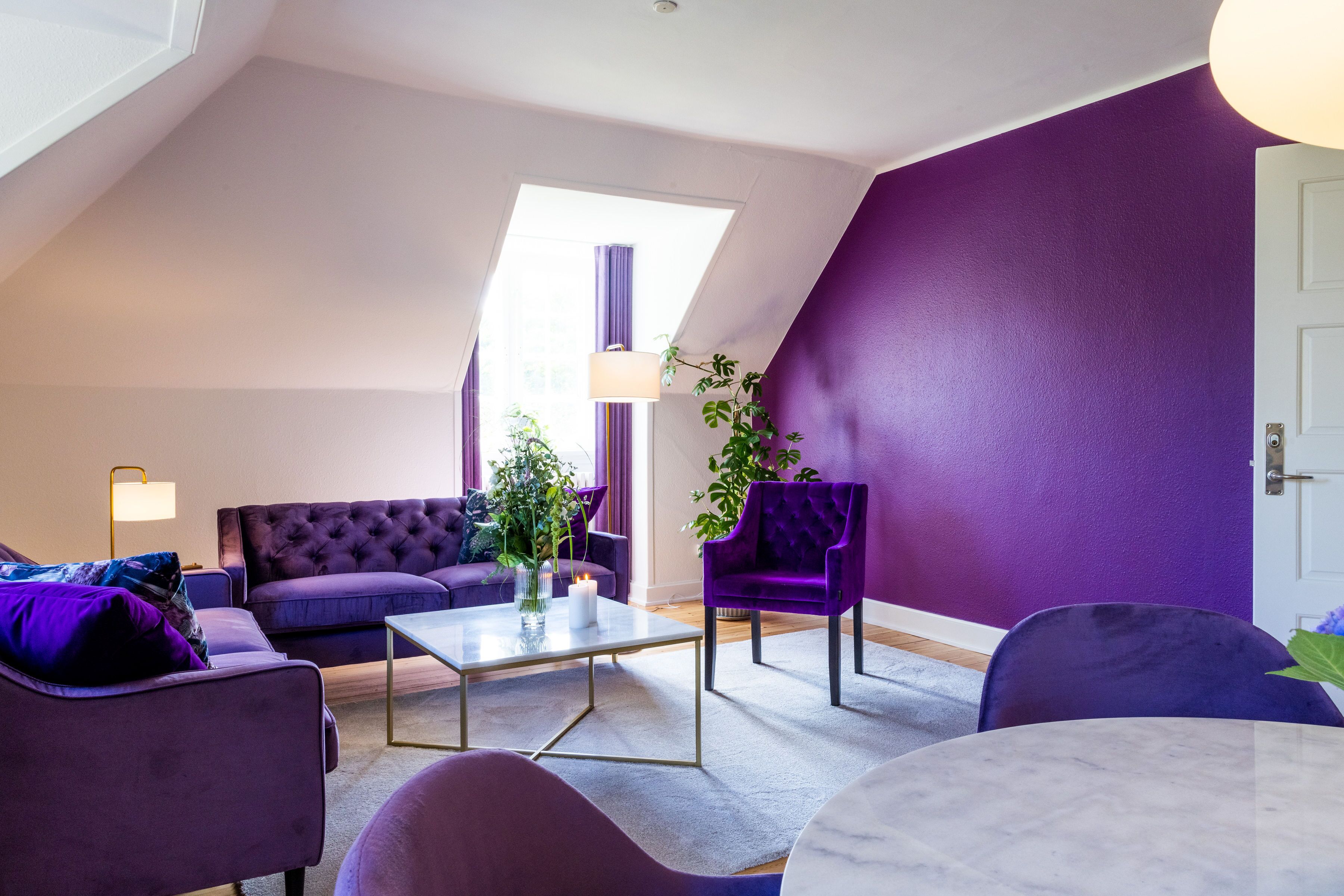 A modern living room with a purple color scheme, featuring a sofa, armchairs, a coffee table, and a lamp.
