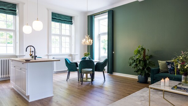 A modern kitchen with a central island, dining area with chairs, a sofa, and a coffee table. - Gem Suites Holiday Apartments (Augustenborg)