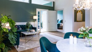 A modern living room with a sofa, a coffee table, and a dining area with chairs and candles. - Gem Suites Holiday Apartments (Augustenborg)