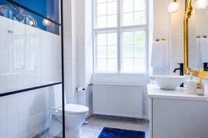 A modern bathroom with a glass shower enclosure, white tiles, a white sink, and a large window.