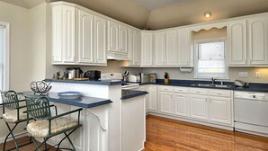 A kitchen with white cabinets, a blue countertop, and a central island with chairs. - 4668- 85 Ocean Blvd, Walk to Beach | Private Pool & Game Room (Southern Shores)