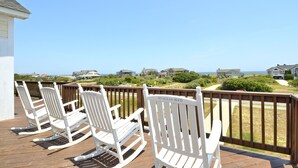 A wooden deck with white rocking chairs facing a scenic view of houses and the ocean. - 4668- 85 Ocean Blvd, Walk to Beach | Private Pool & Game Room (Southern Shores)