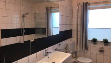 A modern bathroom with a white sink, a toilet, a shower, and a large mirror.