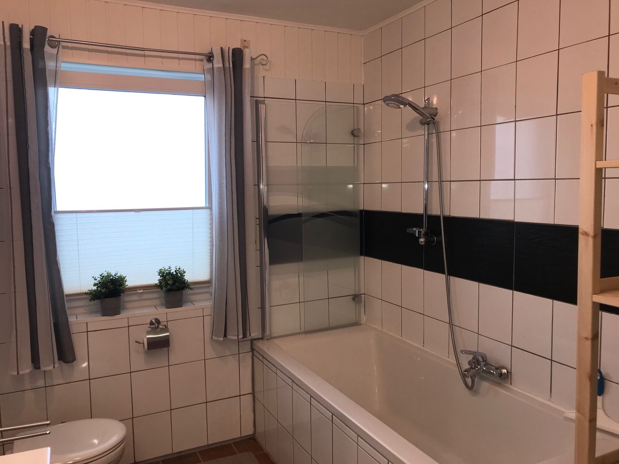 Een badkamer met een douche, toilet en een raam met gordijnen.
