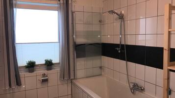 Een badkamer met een douche, toilet en een raam met gordijnen.