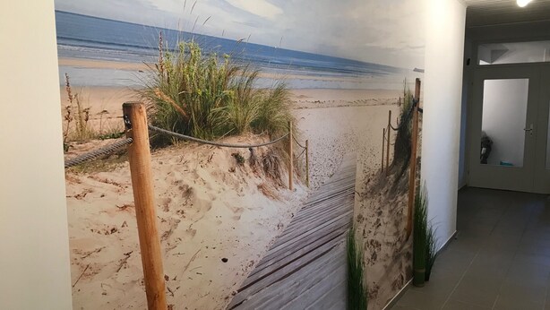 A corridor with a beach mural on the wall, a wooden floor, and a door in the background.