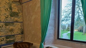 Ein Zimmer mit zwei Ledersesseln, einem Fenster mit Gartenblick und einer Wand mit floralem Muster.