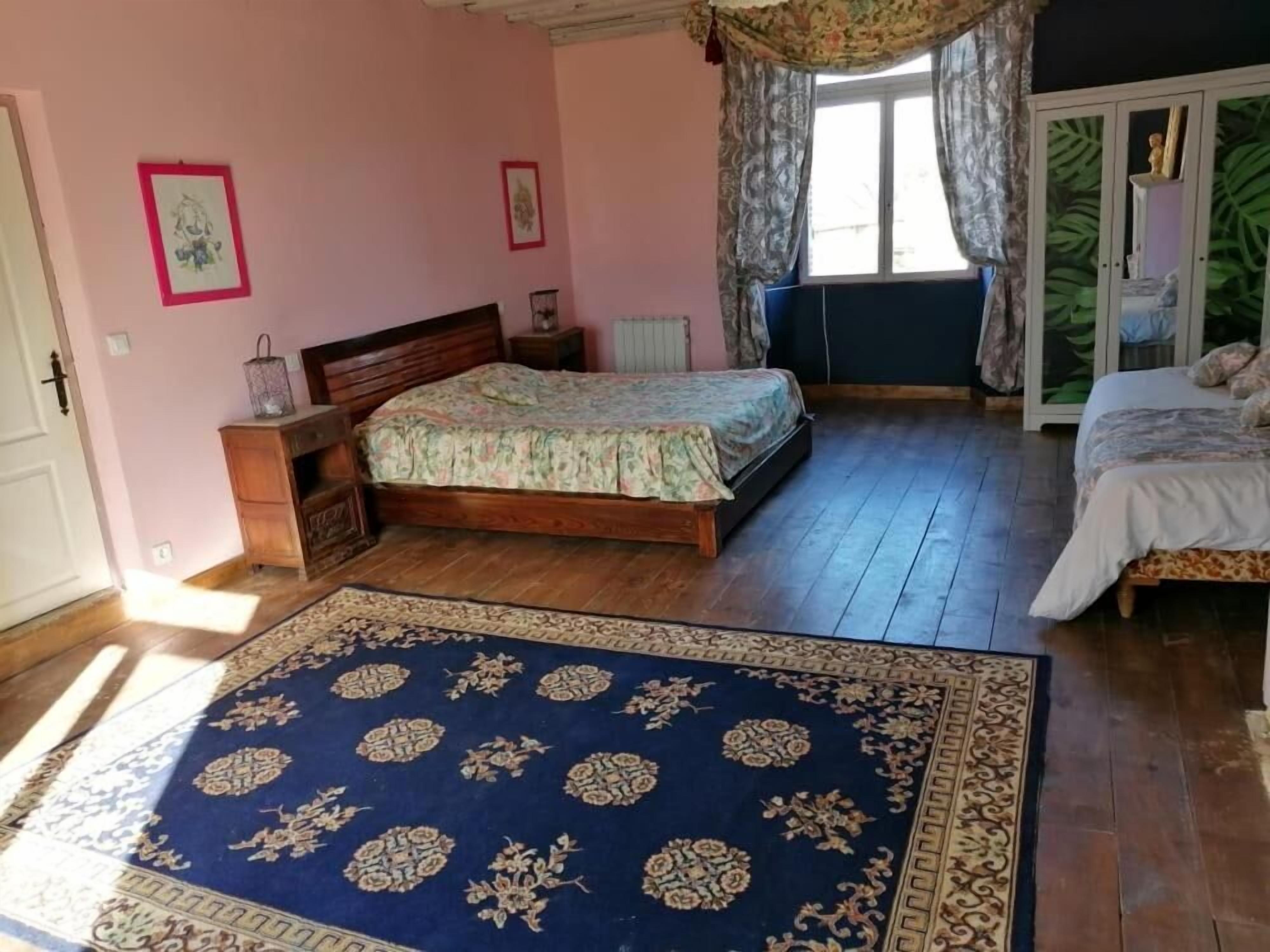 Une chambre à coucher avec un lit en bois, un tapis à motifs bleus et une fenêtre avec des rideaux.
