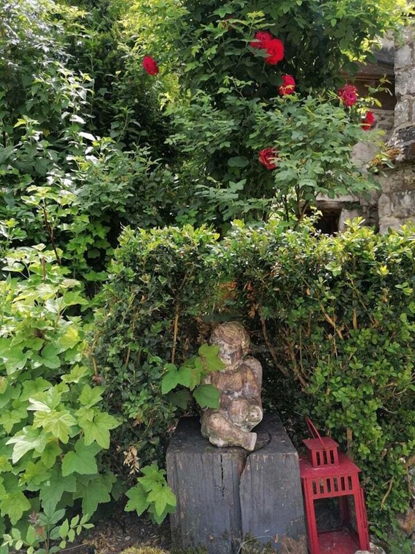 A garden with a stone statue of a seated figure, surrounded by lush greenery and red flowers. - Hôtellerie des Jardiniers Gourmands (Morsains)