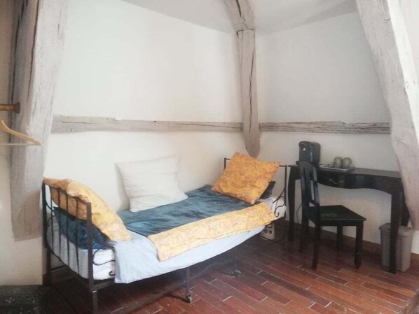 A small, rustic room with a single bed, a wooden desk, and a chair. - Hôtellerie des Jardiniers Gourmands (Morsains)