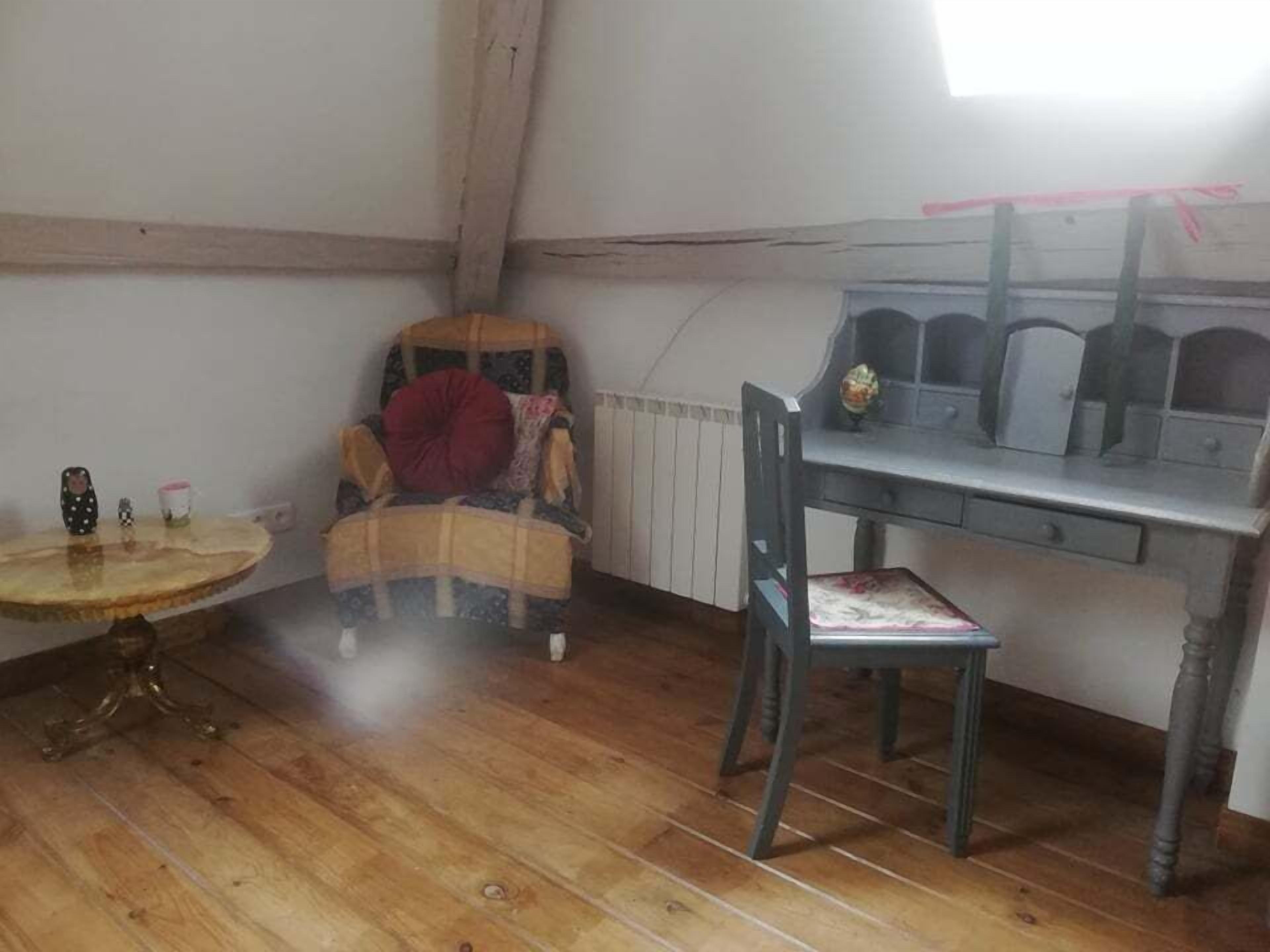 Una habitació petita i acollidora amb terra de fusta, una taula rodona, una cadira amb coixí vermell i un escriptori amb mirall.
