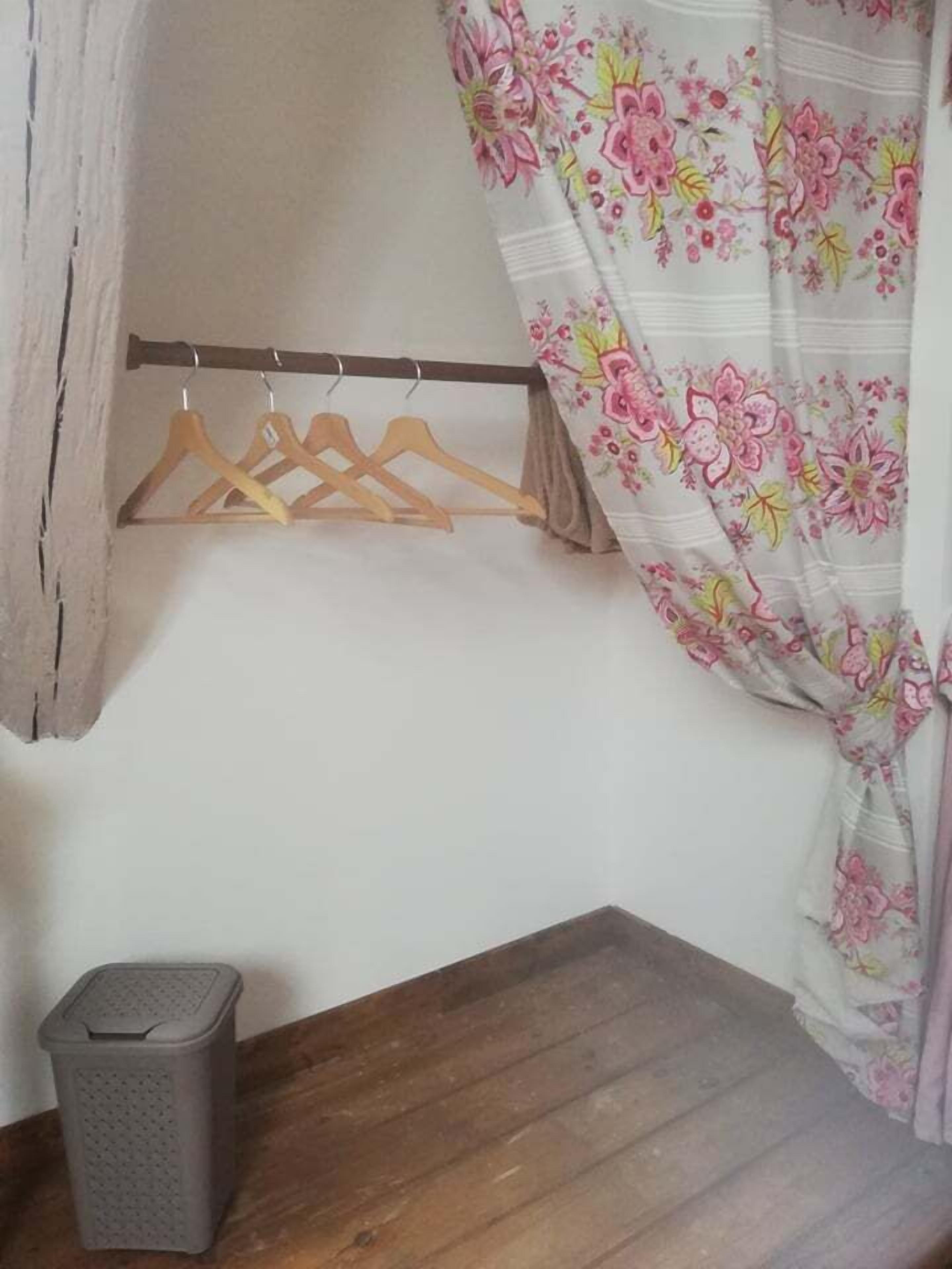 Une petite pièce avec une table en bois, une poubelle, un porte-manteau en bois et un rideau à motifs floraux.