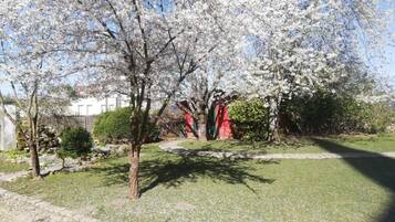 A garden with cherry blossom trees, a stone pathway, and a red building in the background.