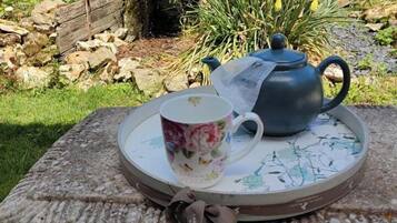 Ein Tisch mit Teekanne und bemalter Tasse auf einer verzierten Ablage im Garten.