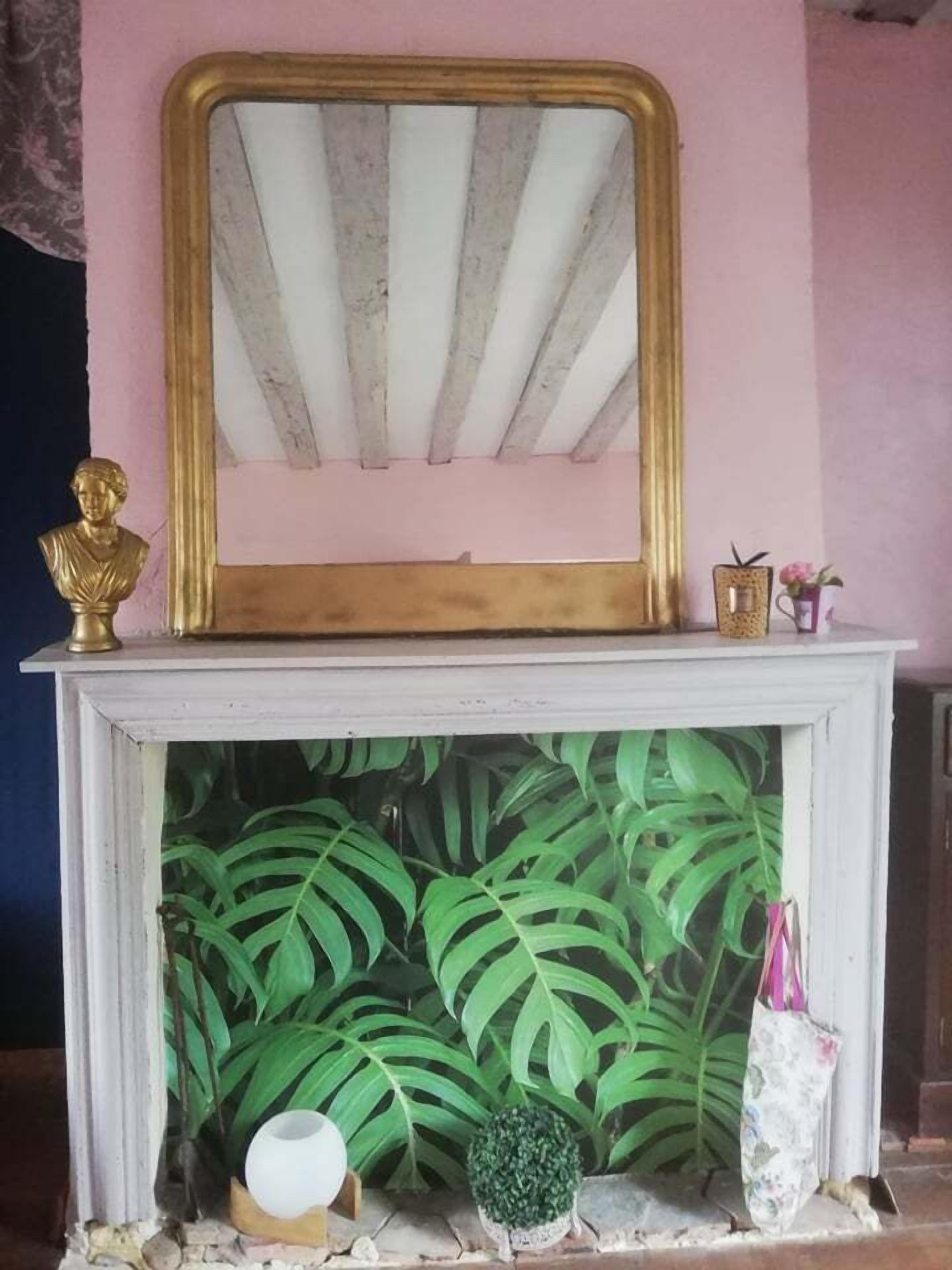 A fireplace with a white mantel, a gold-framed mirror, and a bust sculpture.