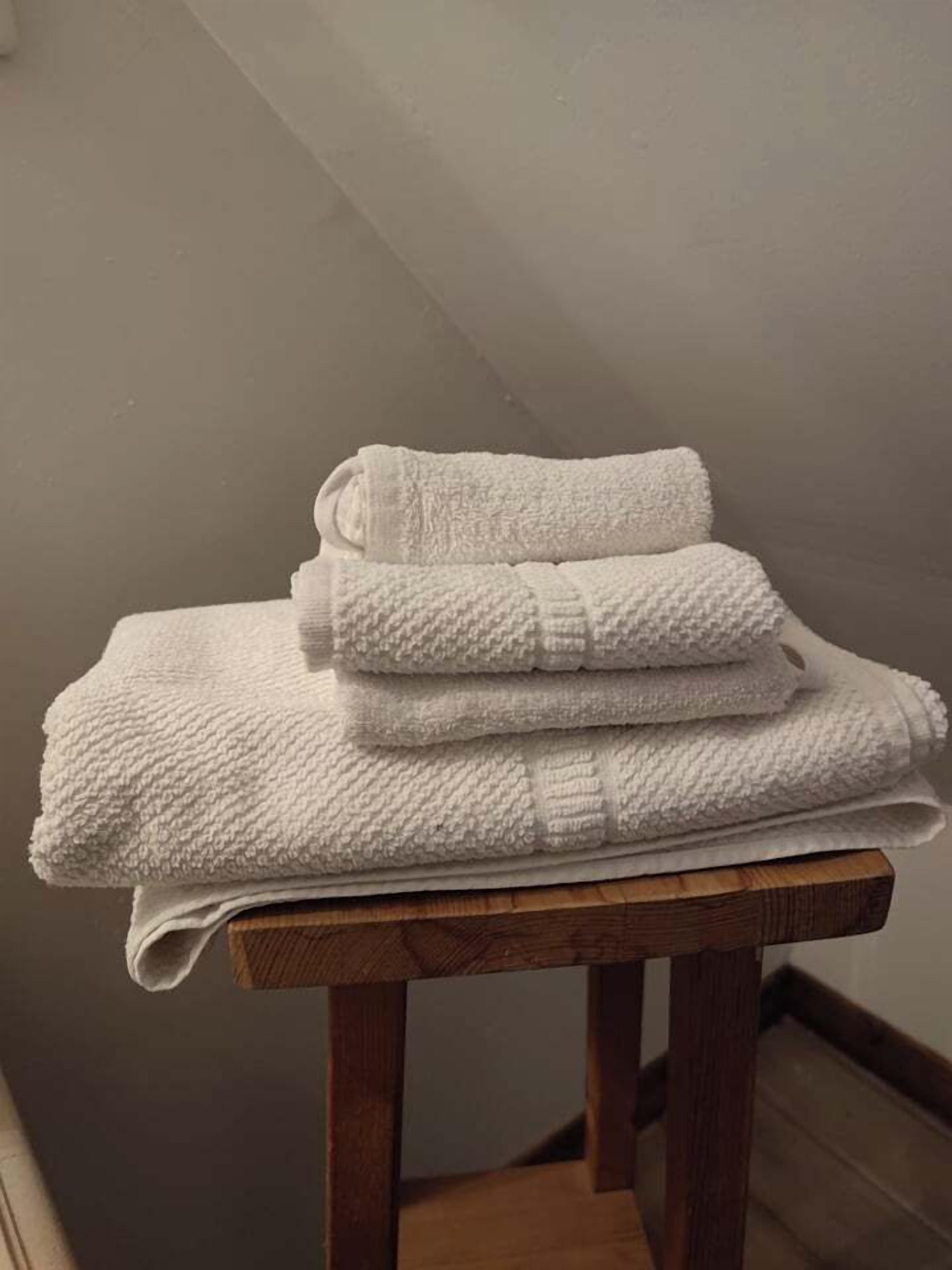 A stack of white towels on a wooden stool in a room with a sloped ceiling.