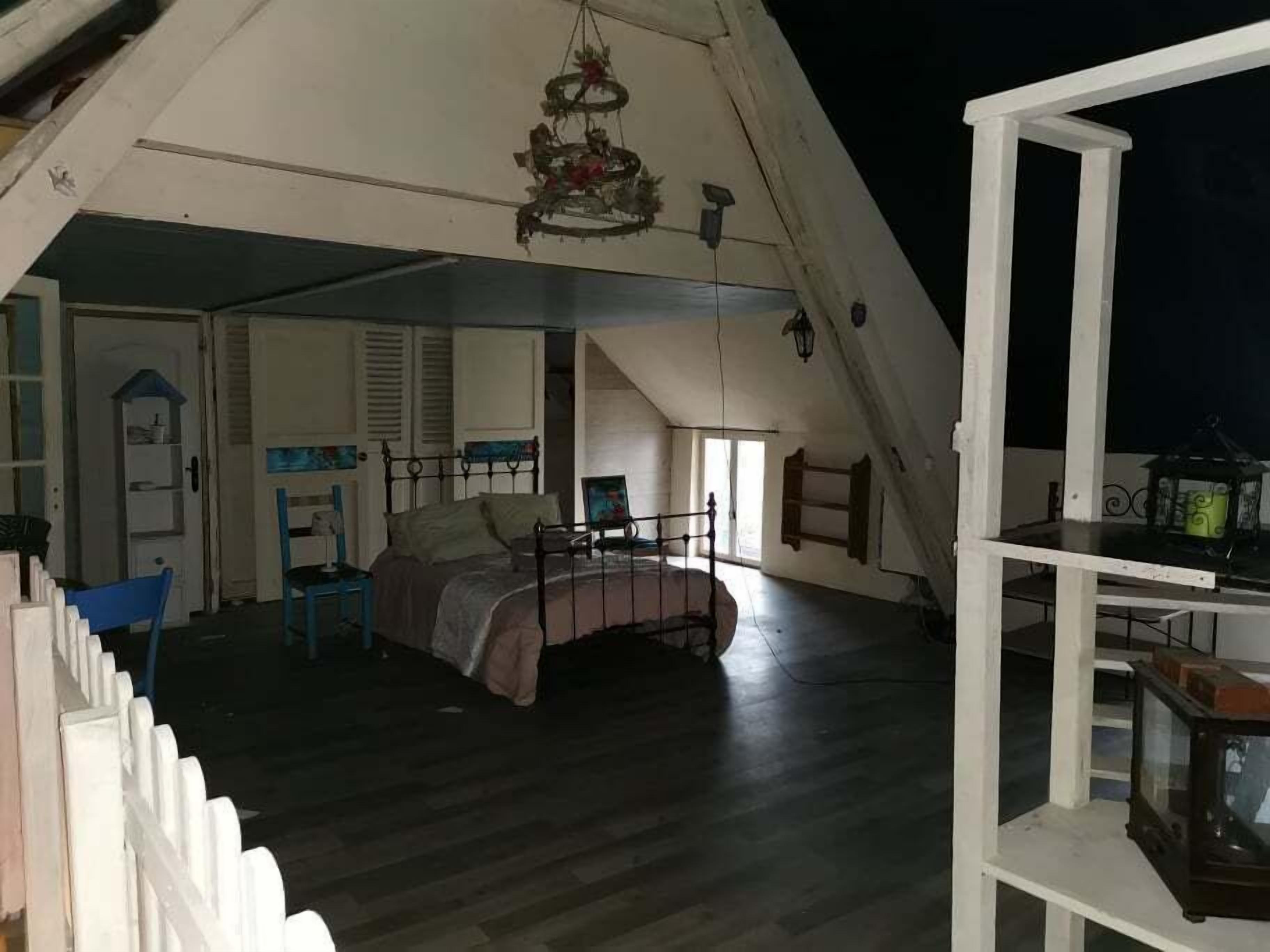 A bedroom with a bed, a chair, a small table, and a hanging light fixture.