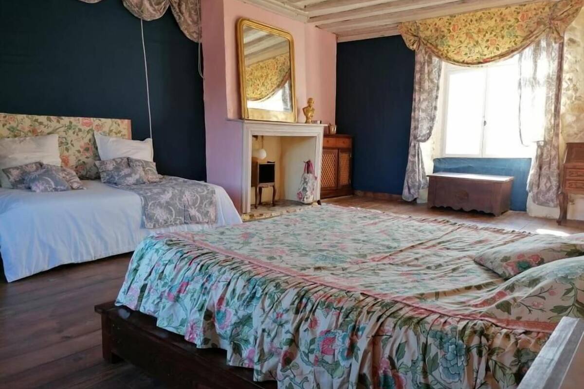 A bedroom with two beds, a large mirror, a fireplace, and a window with curtains.