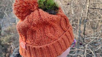 A knitted hat with a pom-pom and a small green moss-like decoration.