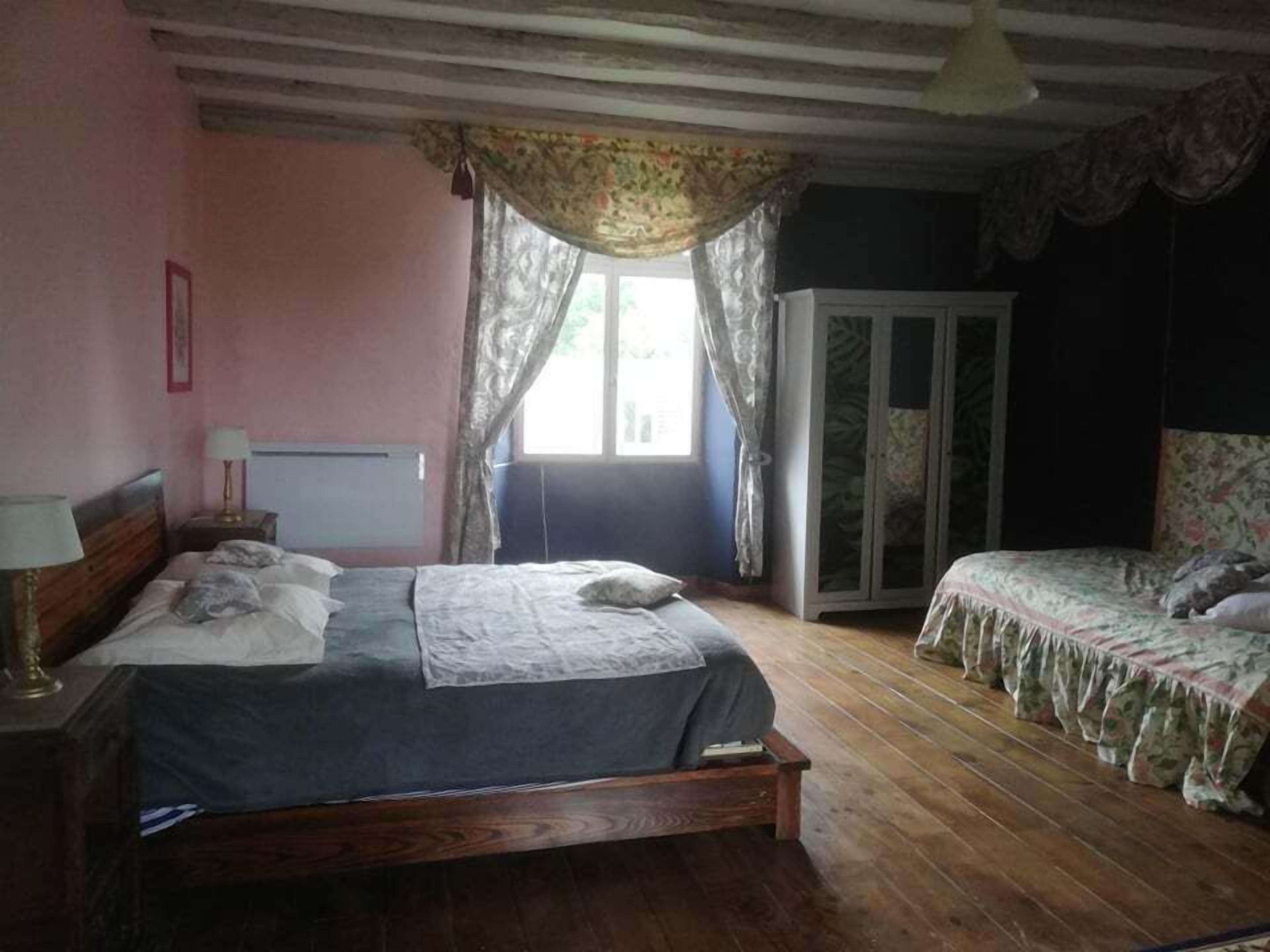 A bedroom with a wooden bed, a smaller bed, a wardrobe, and a window with curtains.
