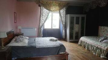 A bedroom with a wooden bed, a smaller bed, a wardrobe, and a window with curtains.