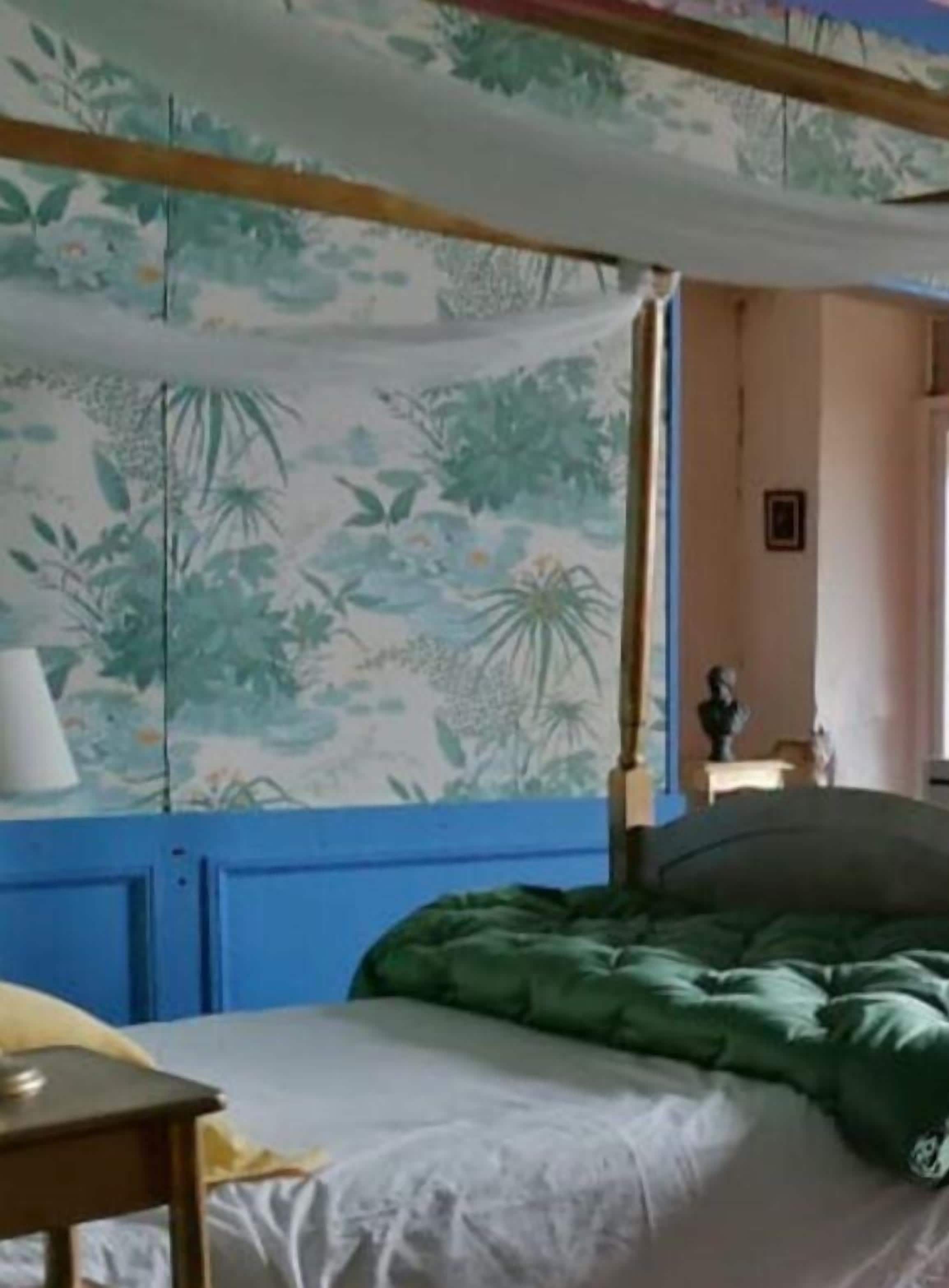 A bedroom with a bed, a nightstand, a lamp, and a wall with a floral pattern.