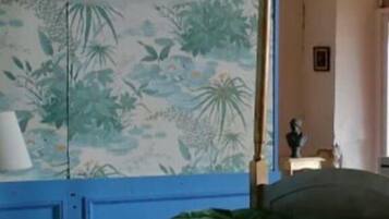 Un dormitorio con cama, mesita de noche, lámpara y pared con estampado floral.