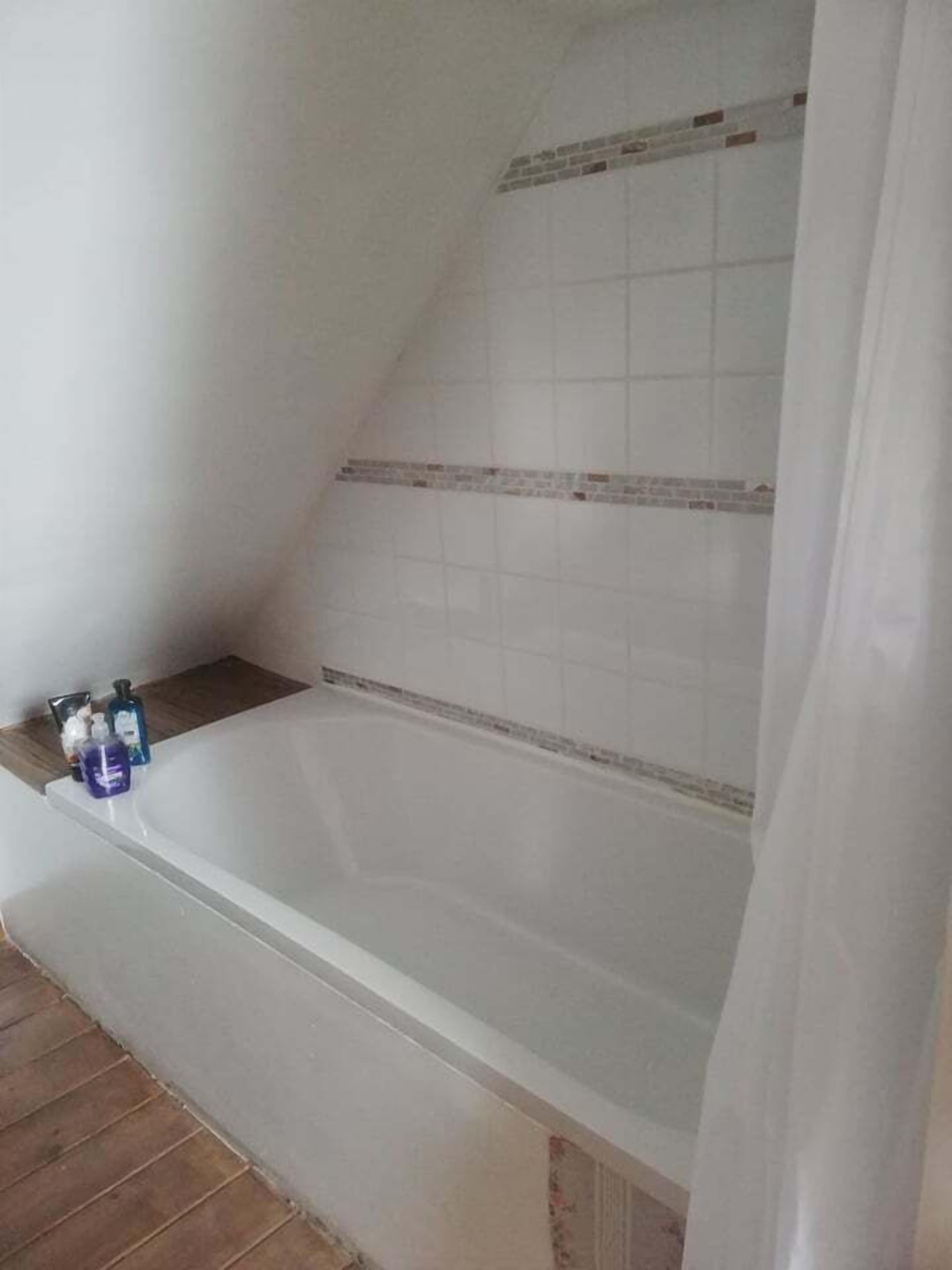 A bathroom with a bathtub, a shower curtain, and toiletries on the side.