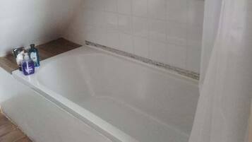 A bathroom with a bathtub, a shower curtain, and toiletries on the side.